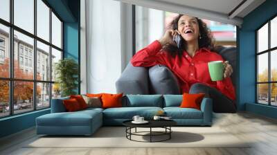 \Happy and smiling latin woman sitting on sofa and using internet on computer with smart mobile phone in living room. Lifestyle with technology Wall mural